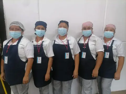 Personal de cocina uniformado, con cofia y cubrebocas, en las instalaciones de un cliente